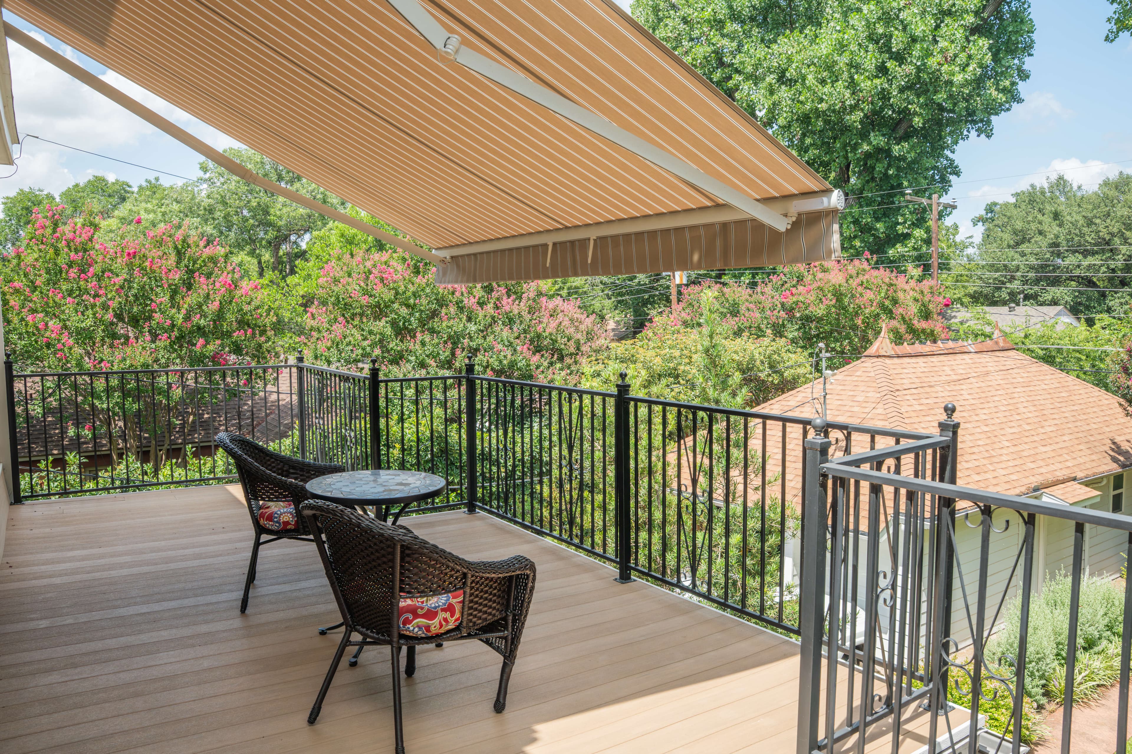 Beige-striped retractable awning shading an elevated deck with wicker bistro furniture