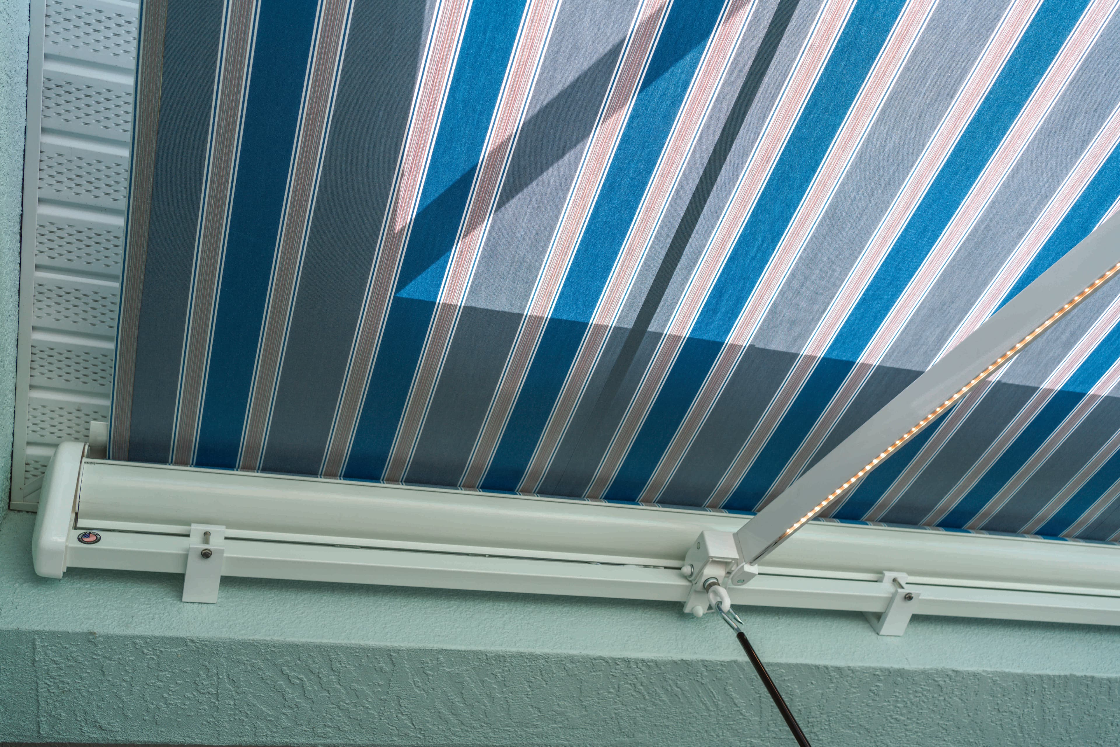 White-frame SunPro retractable awning with striped fabric and LED lighting shading a deck
