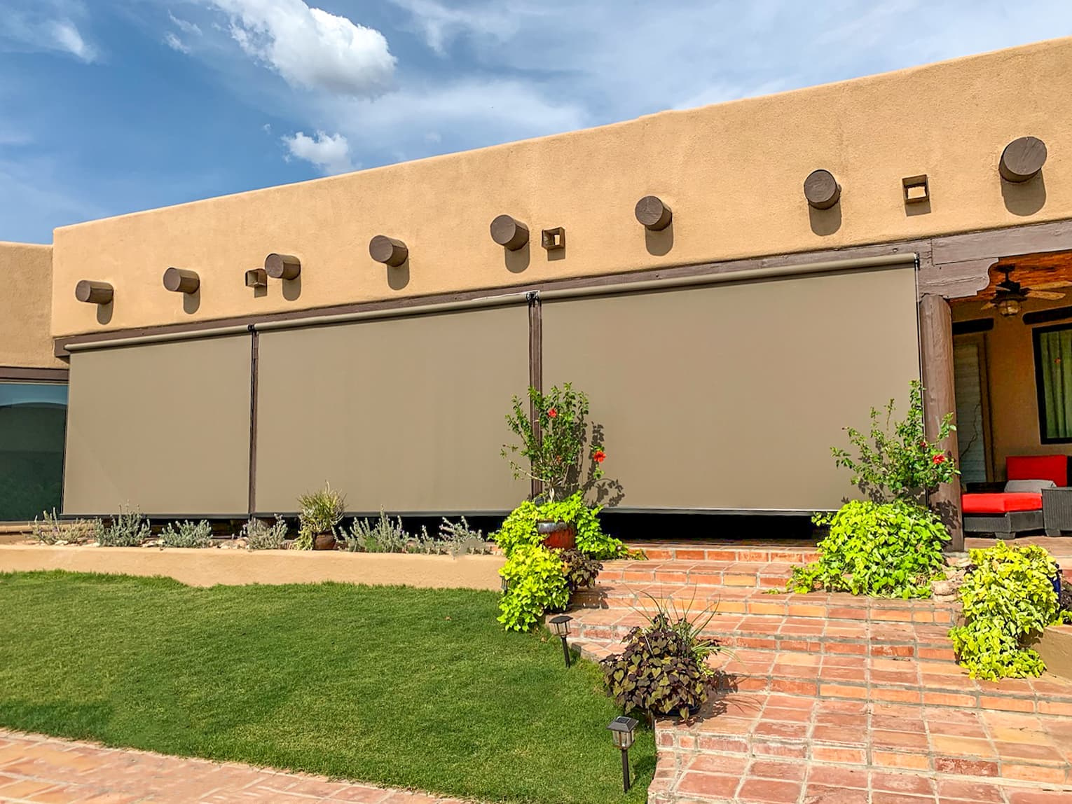 Beige open-roller solar screens enclosing a Southwest-style patio under a desert sky