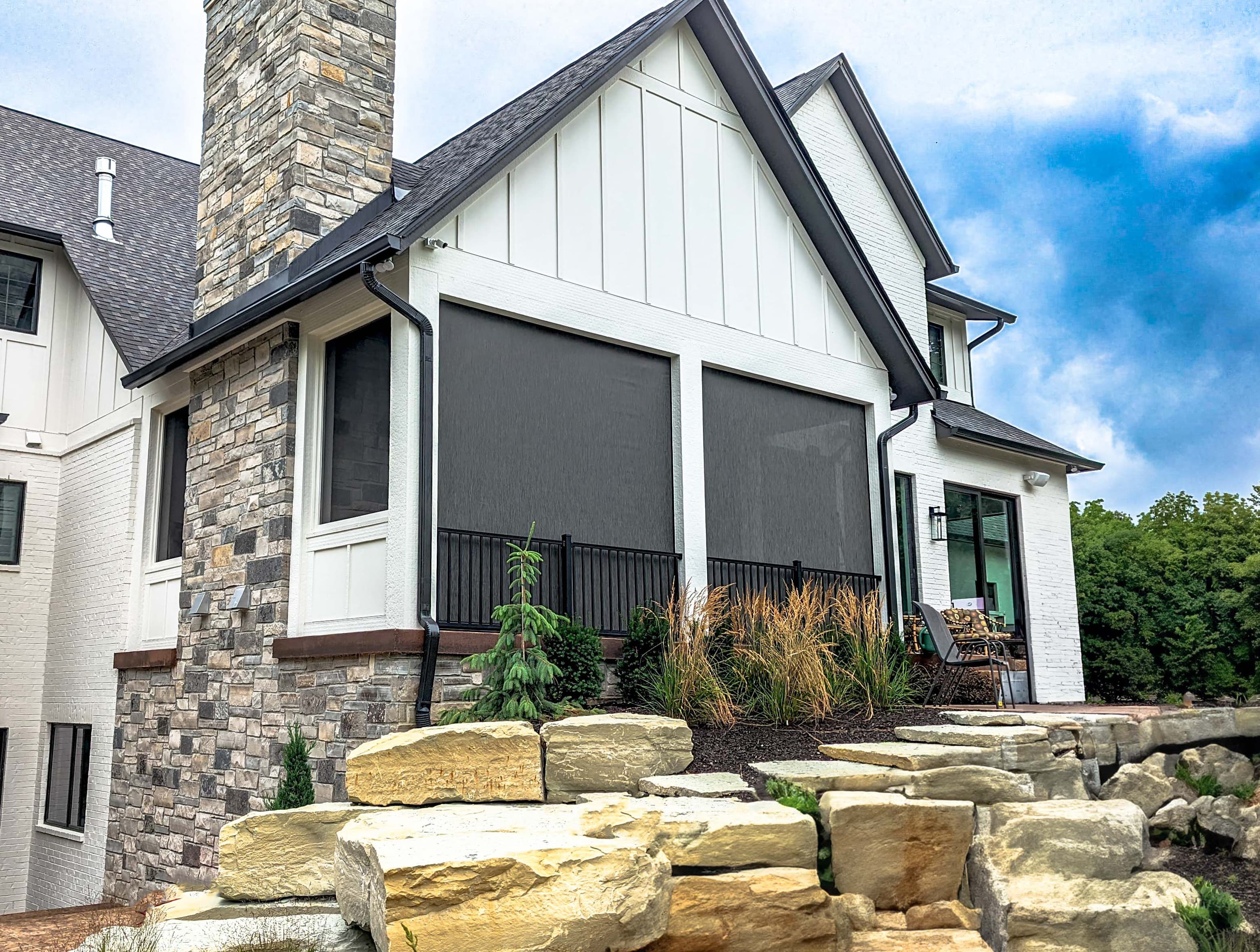 Recessed solar screens lowered across the rear porch openings of a modern white farmhouse