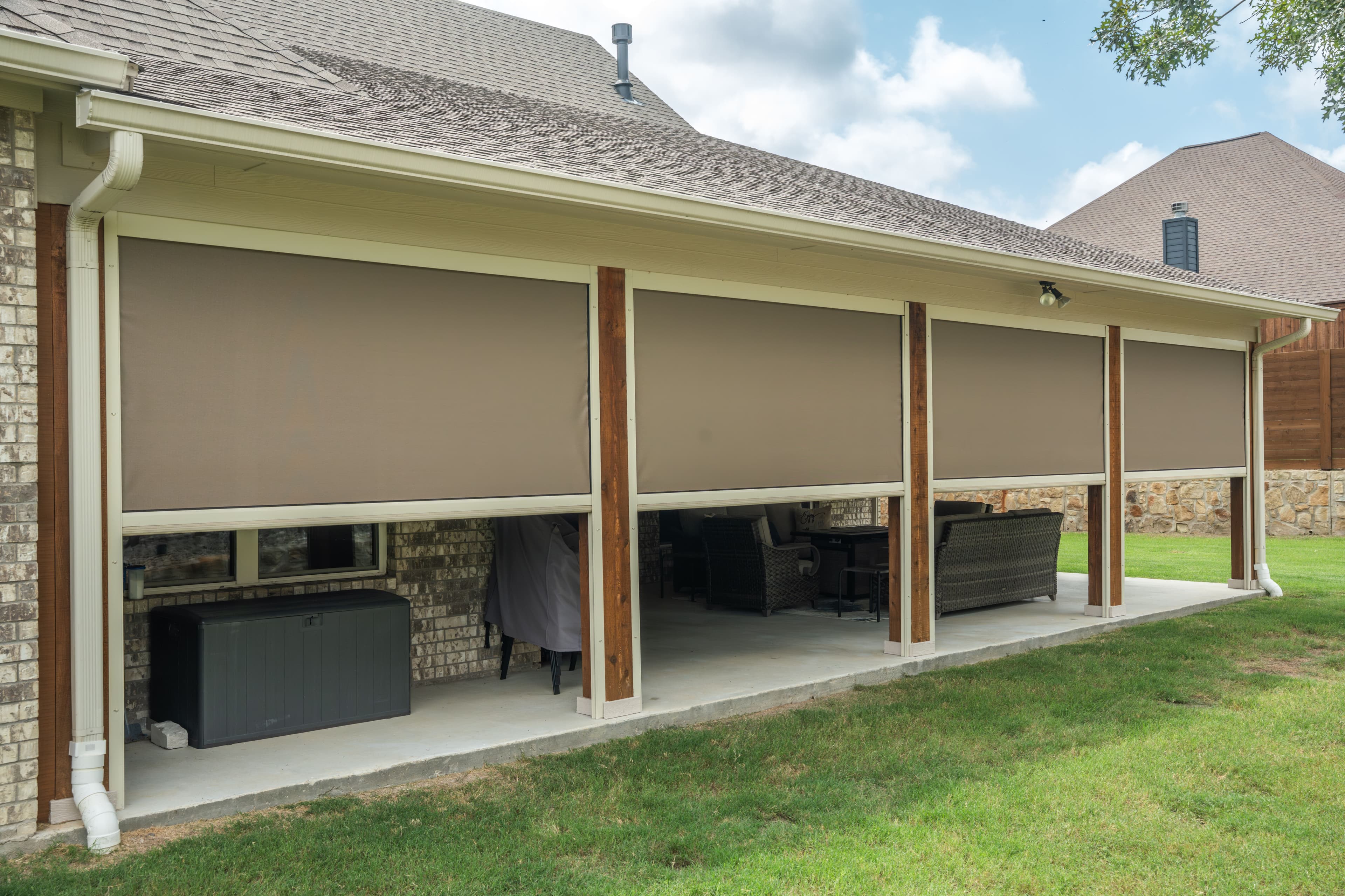 Row of beige motorized screens with white hardware enclosing a long covered patio on a brick home